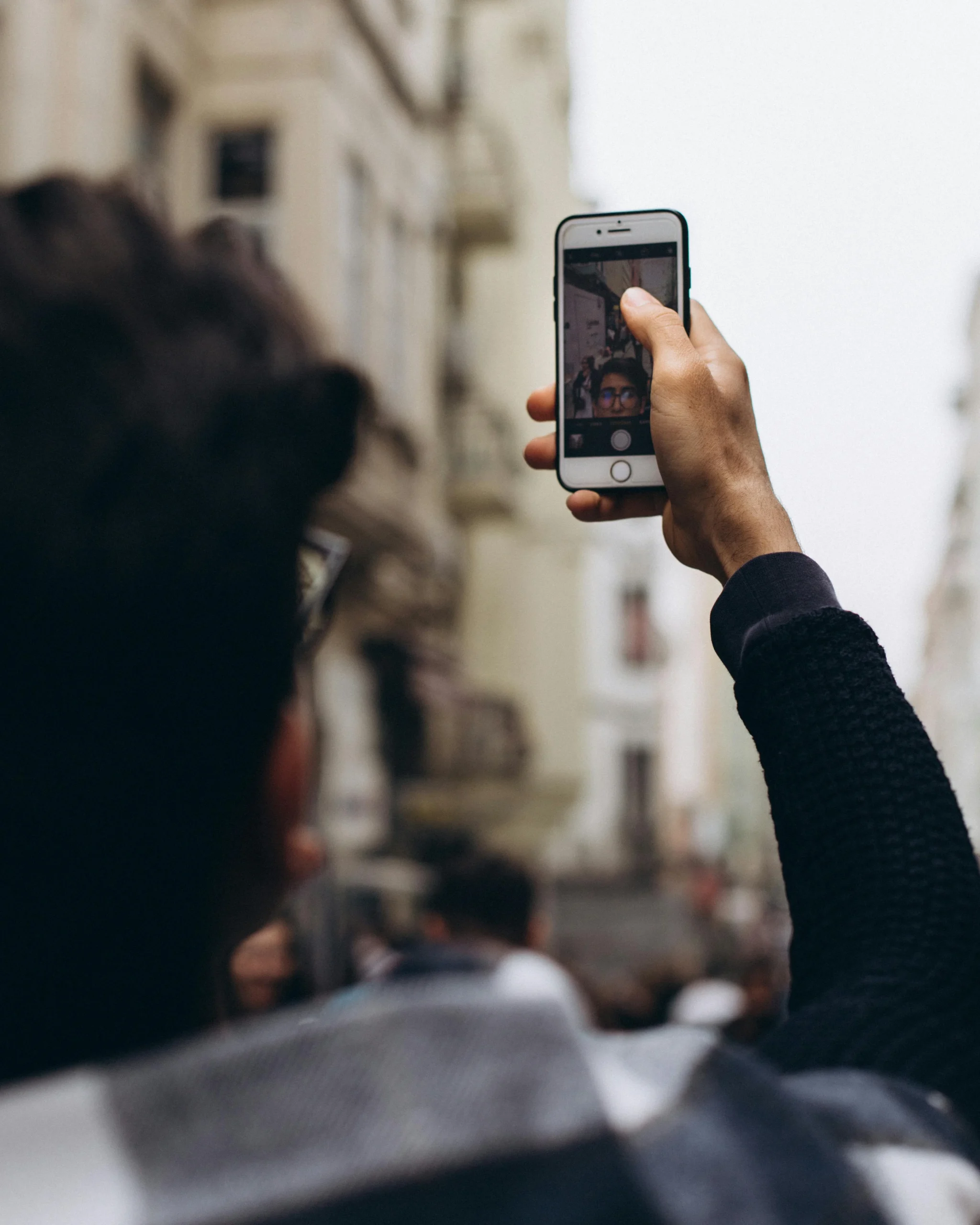 Person taking ID photo with smartphone against plain wall